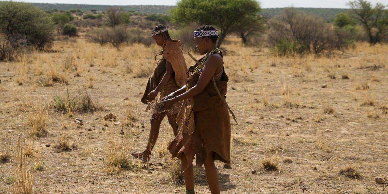 African women wearing traditional leather clothes while walking on dry grass