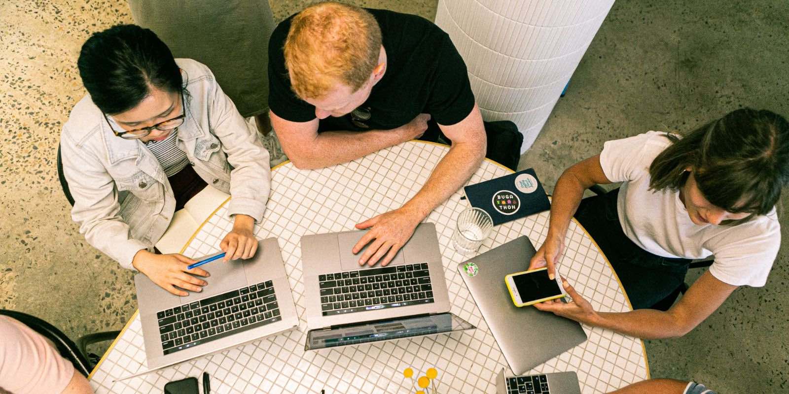 a group sitting in a round table using their phone and laptops