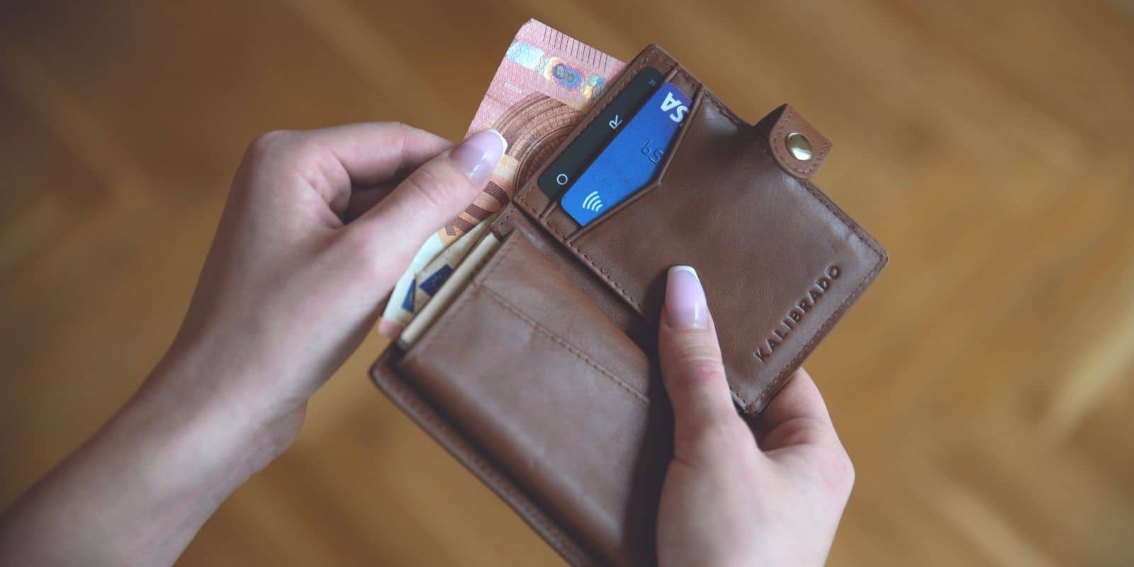 a woman's hand pulling out money from her brown wallet