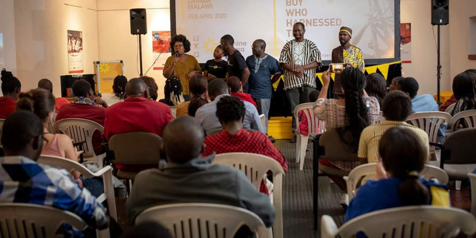 a group of people presenting in front with listeners sitting