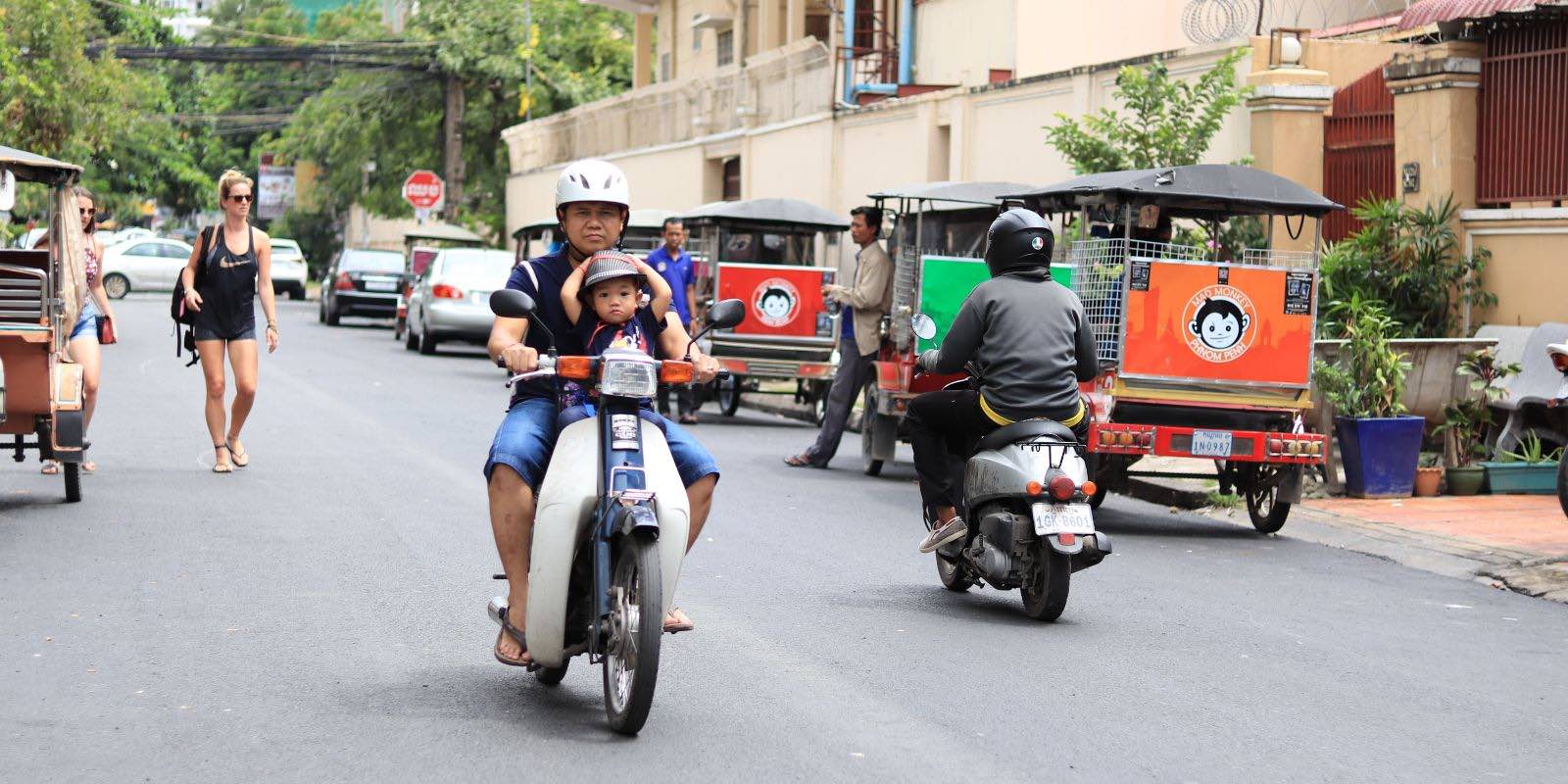 locals riding motorcycles and tourists walking in a street in Cambodia