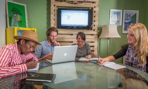 a group of people sitting around a table working on laptops