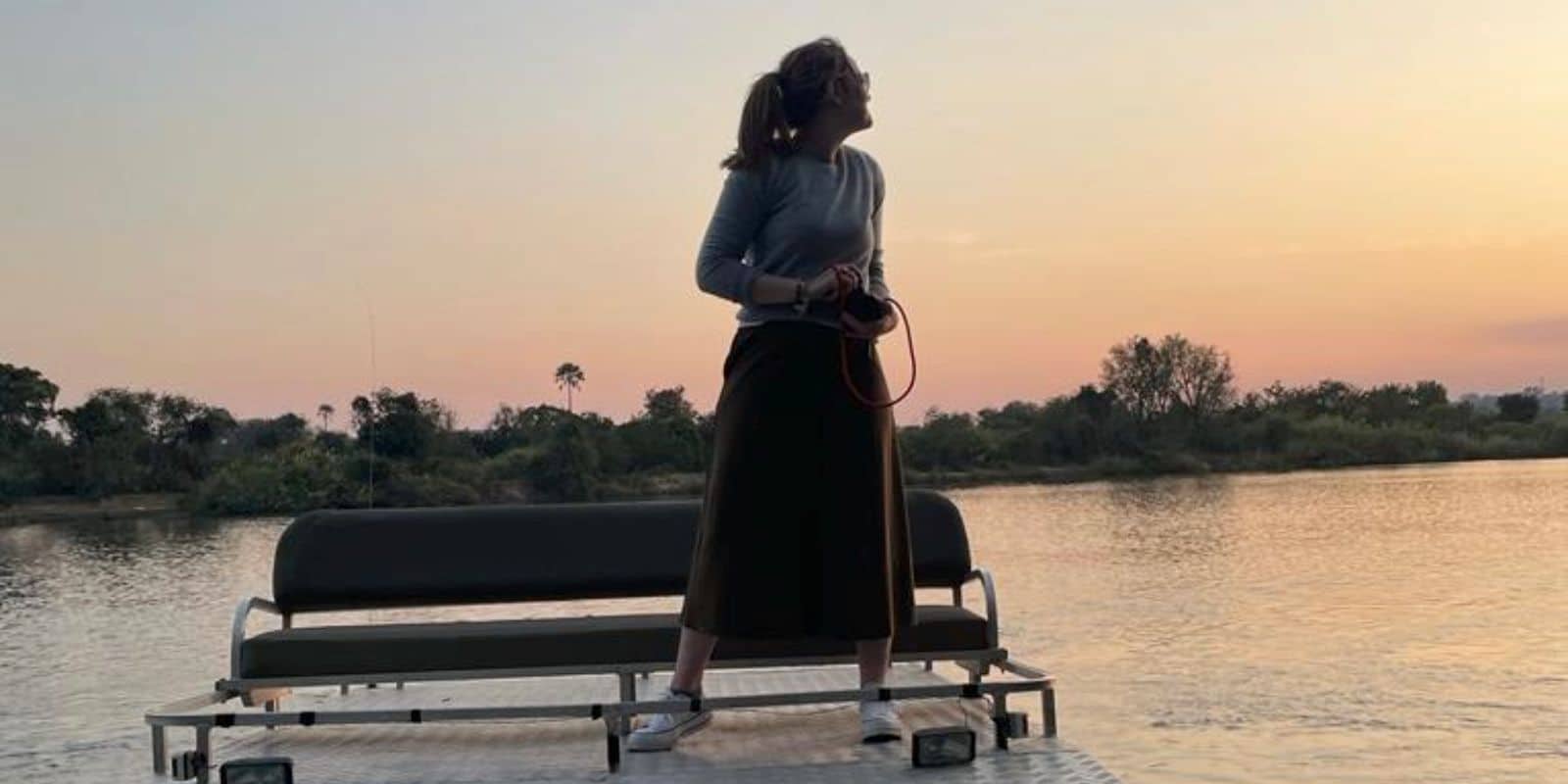 a woman standing on a pontoon boat at sunset
