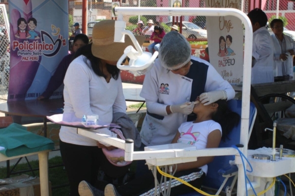 a dentist checking a young girl's teeth in an outdoor medical mission