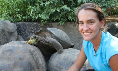 a woman smiling while feeding a tortoise