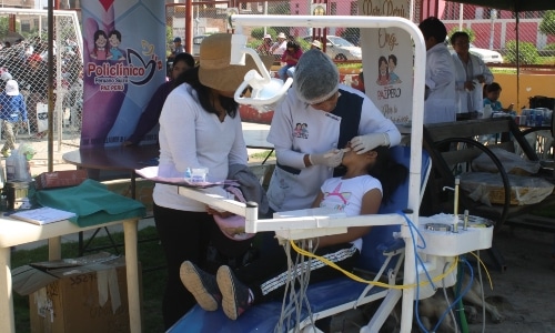 a dentist checking a young girl's teeth in an outdoor medical mission