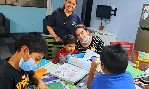 A woman with a face mask and children at a table