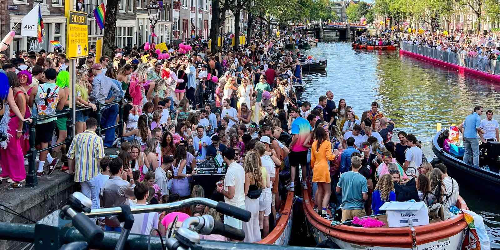 people gathered along the river in Amsterdam, with several individuals riding in boats