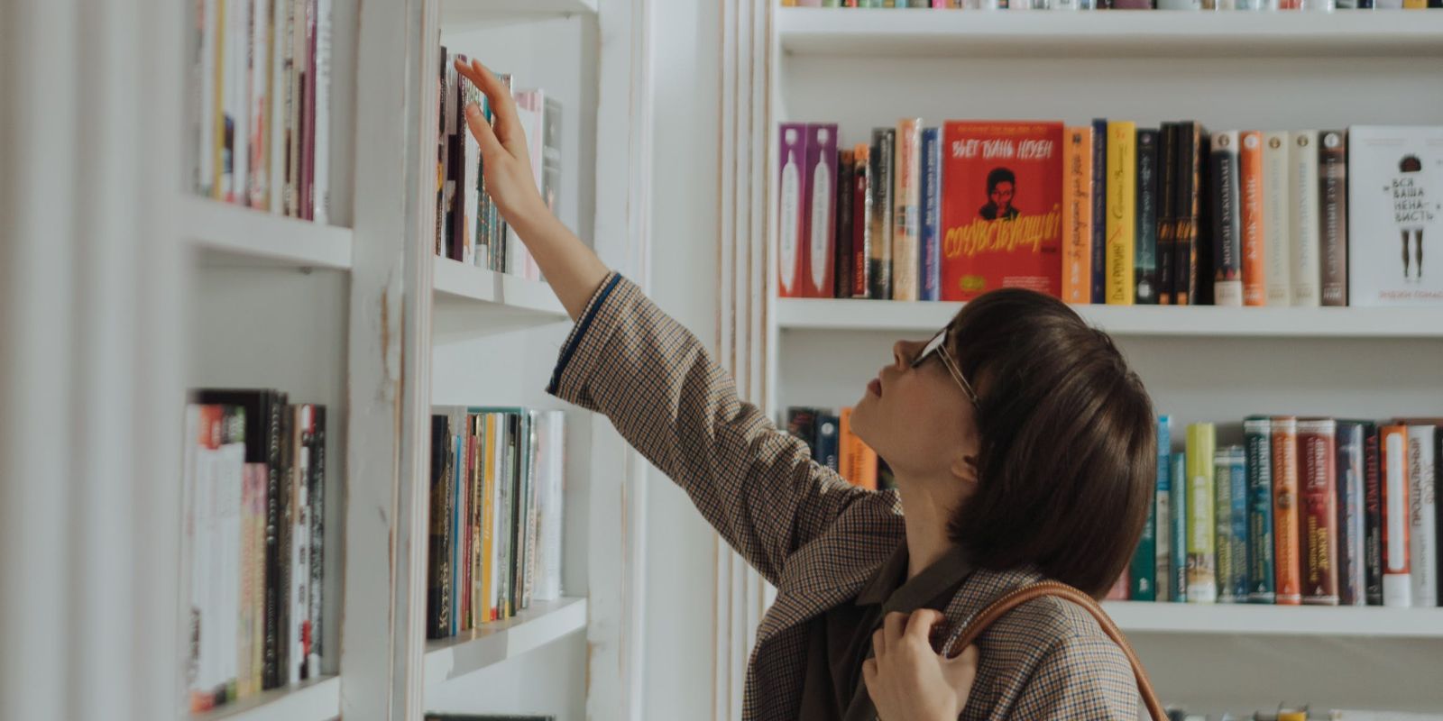 woman picking books in front of a book shelf
