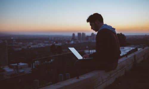 a man sitting on top of a building with a laptop on his lap