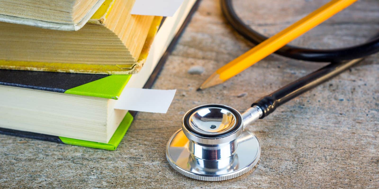a book, stethoscope and pencil laid on top of the table