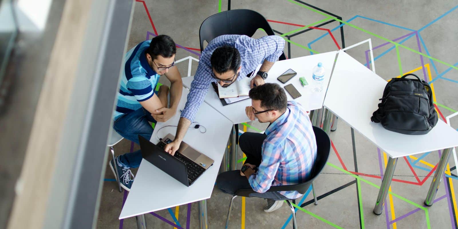 top-view photo of 3 men discussing while using a laptop