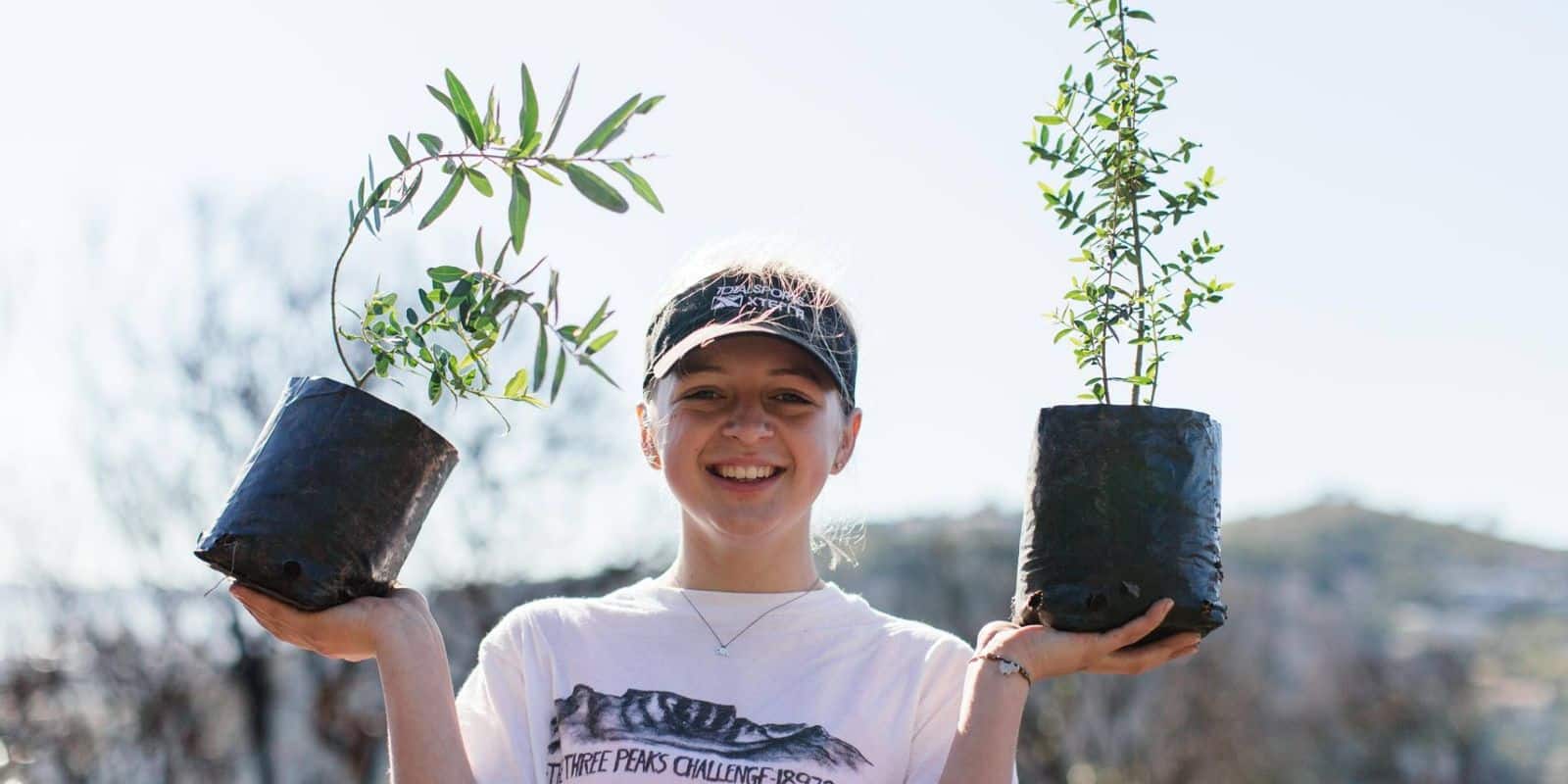 Volunteer smiling and holding two plants in her hands.