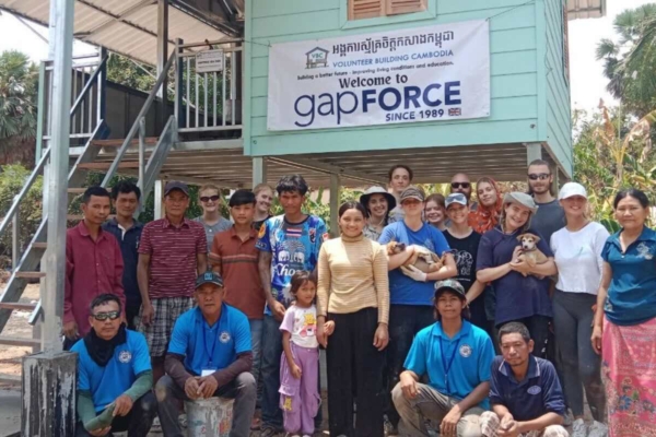 group of volunteers and locals posing in front of a building with a sign reading "Welcome to gapFORCE"