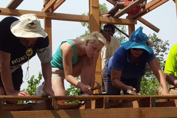 volunteers working on a wooden construction project, hammering nails into the structure, with one volunteer wearing a wide-brimmed hat