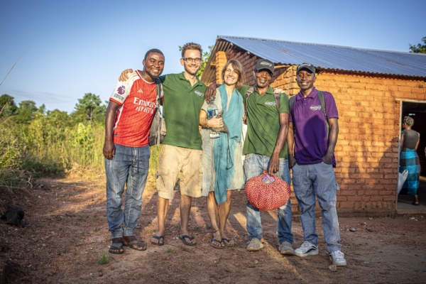 A diverse group of agroforestry interns and local Malawians smiling together outside a rural building after a productive day of work.