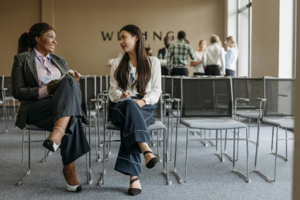 Two interns in Europe chat in a conference room during their communications internship, with colleagues in the background.