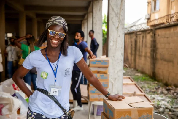 A smiling volunteer stands next to aid boxes during a distribution event.