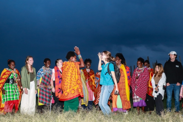 A group of people, including locals in traditional attire, gather outdoors, engaging in a cultural exchange.