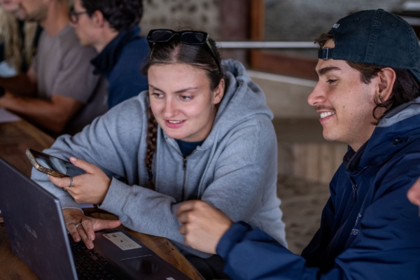 Two individuals collaborating on a laptop, working on what appears to be wildlife data or research in a rustic environment.