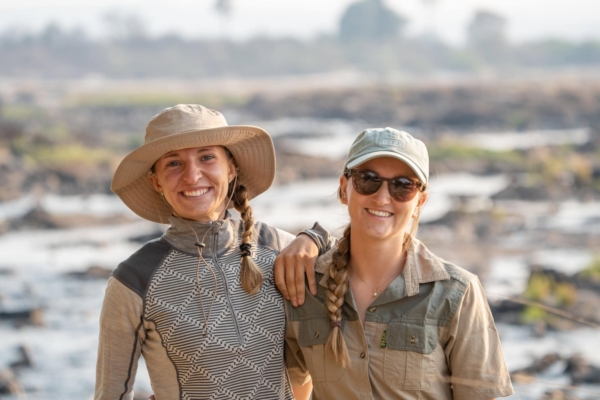 Two ladies posing for a picture in front of a river.