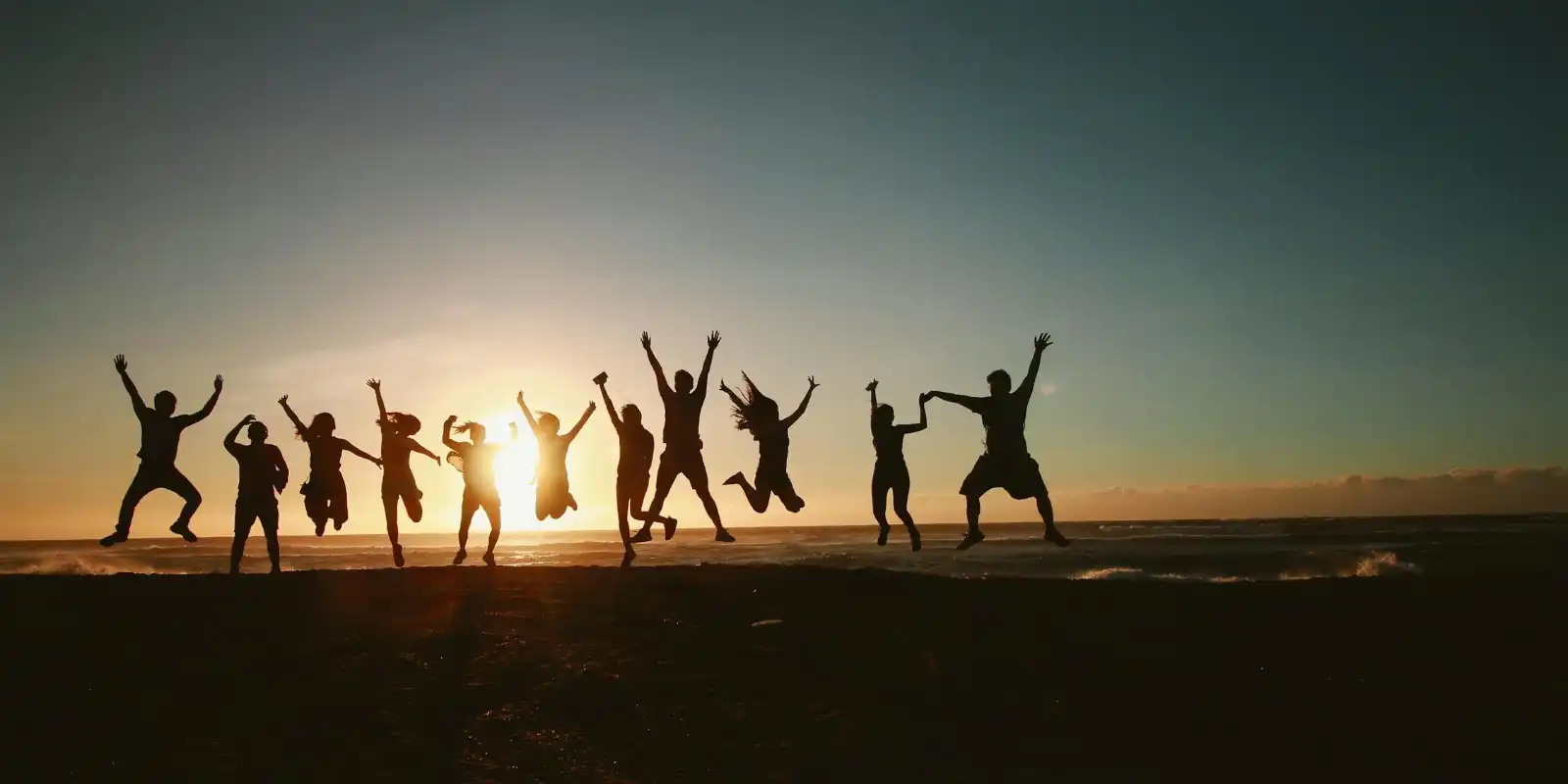 A group of people jumping in a beach at sunset, silhouetted against the sky