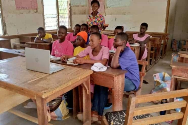 Girls engage in a digital learning session using a laptop in a classroom, guided by a mentor in an inspiring tech education setting.