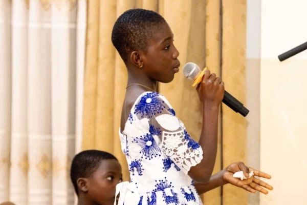 A confident young girl speaks into a microphone during a session, developing public speaking and leadership skills.
