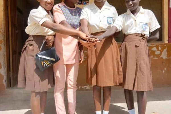 A group of girls in uniform join hands with a mentor outside their school, symbolizing unity, sisterhood, and empowerment through education.