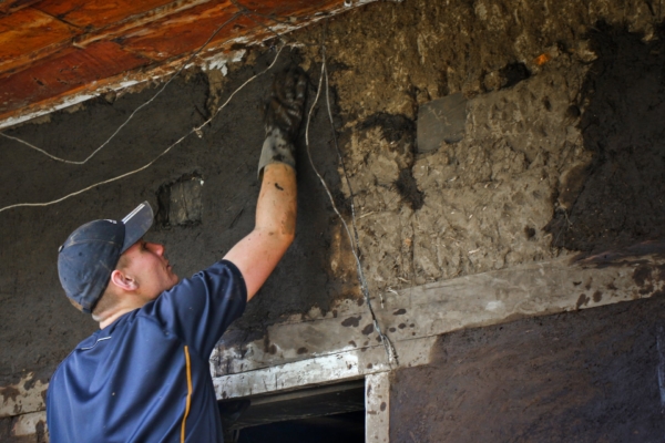 An intern applies a natural mud mixture to reinforce a wall.