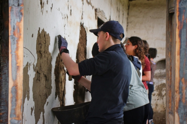 Interns apply earthen plaster to repair and insulate a building wall.