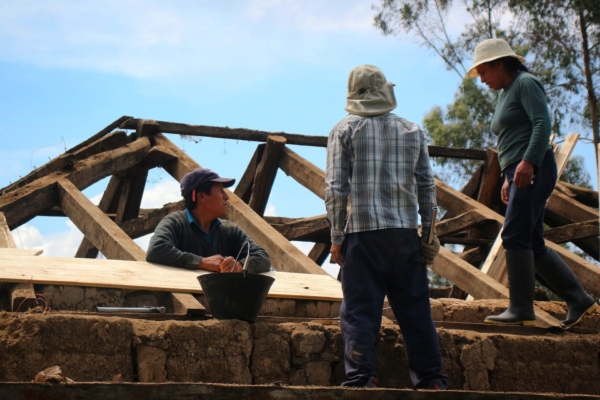 Local builders assess wooden beams during roof construction.