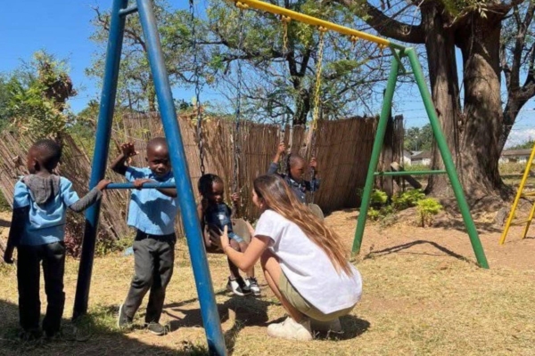 A medical intern playing with the children by the swing set.