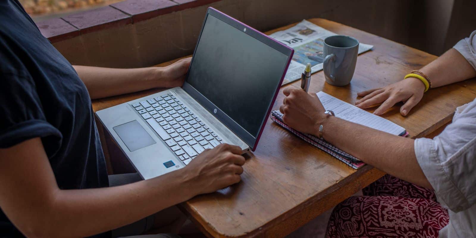 Close-up of two women working with a laptop and notebook