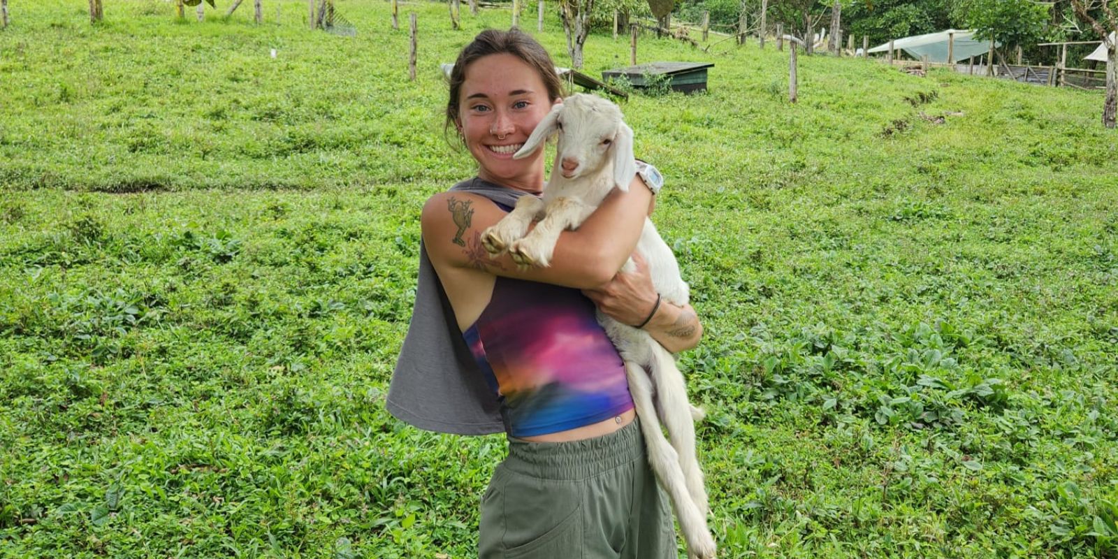 Person smiling while holding a small white goat in a green field