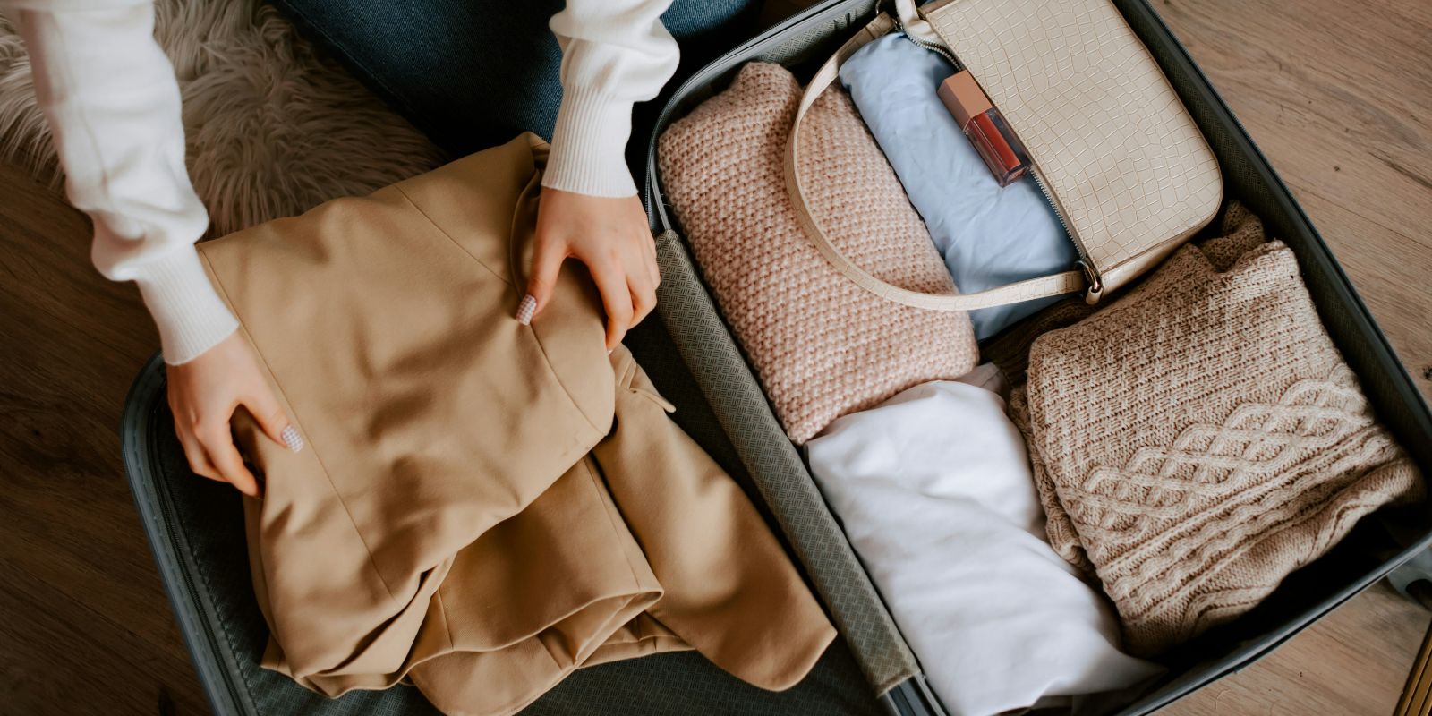 Person packing neatly folded clothes and a bag inside a suitcase