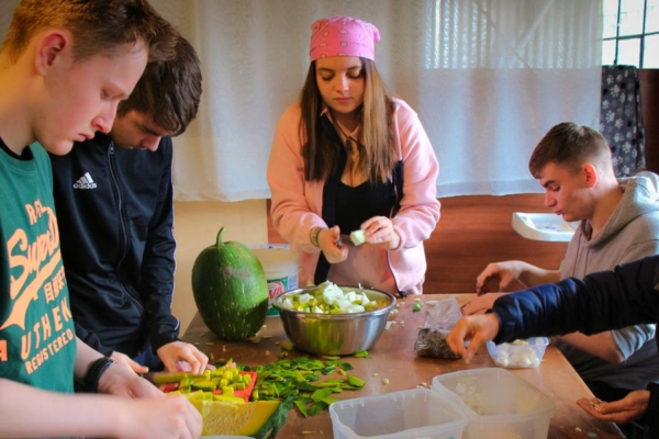 Group of people preparing food together at a table inside a shared kitchen space