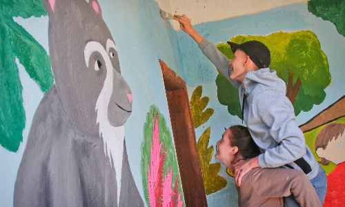 Two people painting a colorful mural on a wall featuring animals and nature scenes