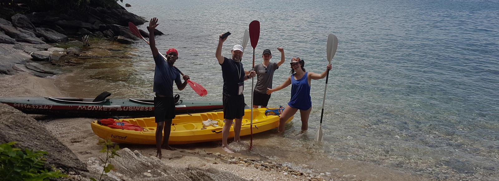 Four people standing near a kayak on the beach.