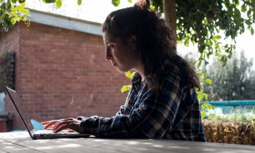 a woman using a laptop at an outdoor table