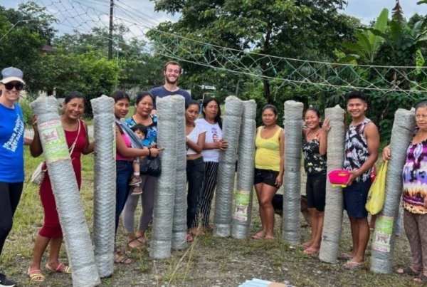 interns smiling with a group of community members holding materials for a chicken coop