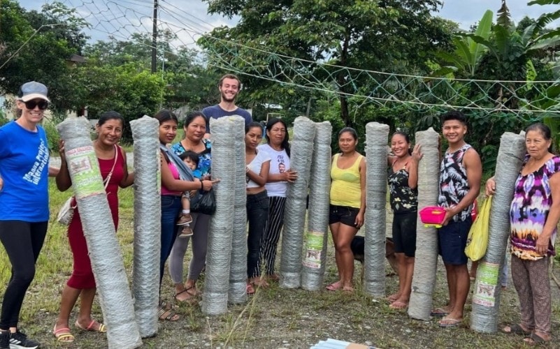interns smiling with a group of community members holding materials for a chicken coop