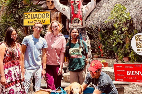 Diverse group posing near an Ecuador equator sign with a dog during a young womens health internship.