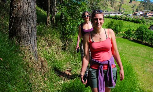 Two people walking along a grassy path through a green hillside on a sunny day