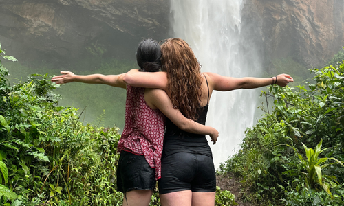 Two women with their arms around each other near a waterfall.