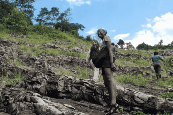 Four people hiking up a hill. One person has turned back to make a peace sign with her hand.
