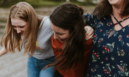 Three girls laughing with their arms around one another.