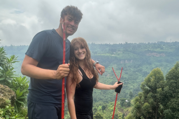 Two people holding sticks posing for a photo on a tall hill.