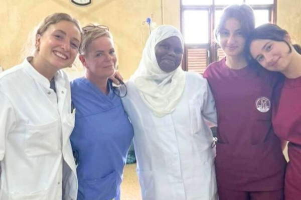 Five women wearing scrubs with their arms around one another.