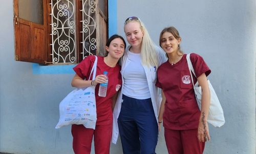 Three smiling women wearing scrubs. Two of them have tote bags.